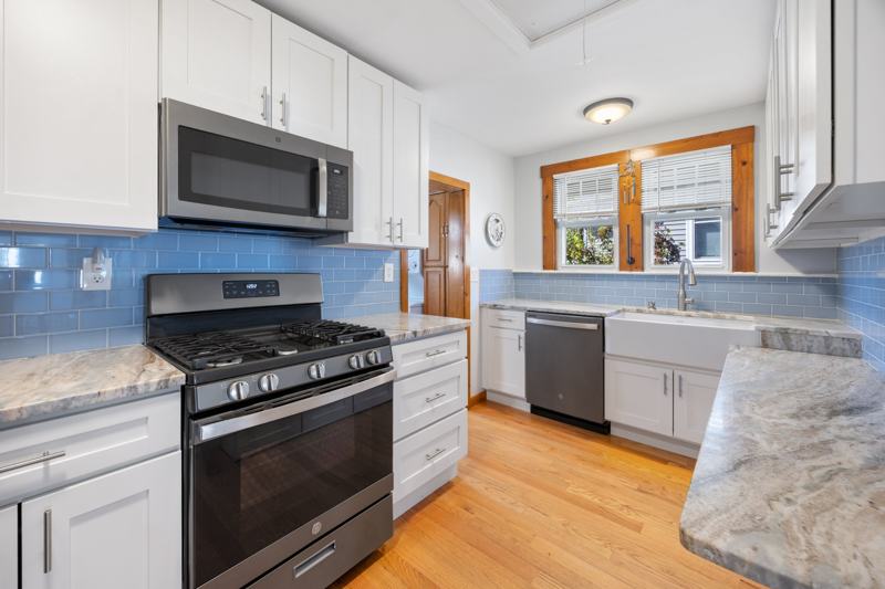 Updated kitchen with white cabinets, blue subway tile, and gas range
